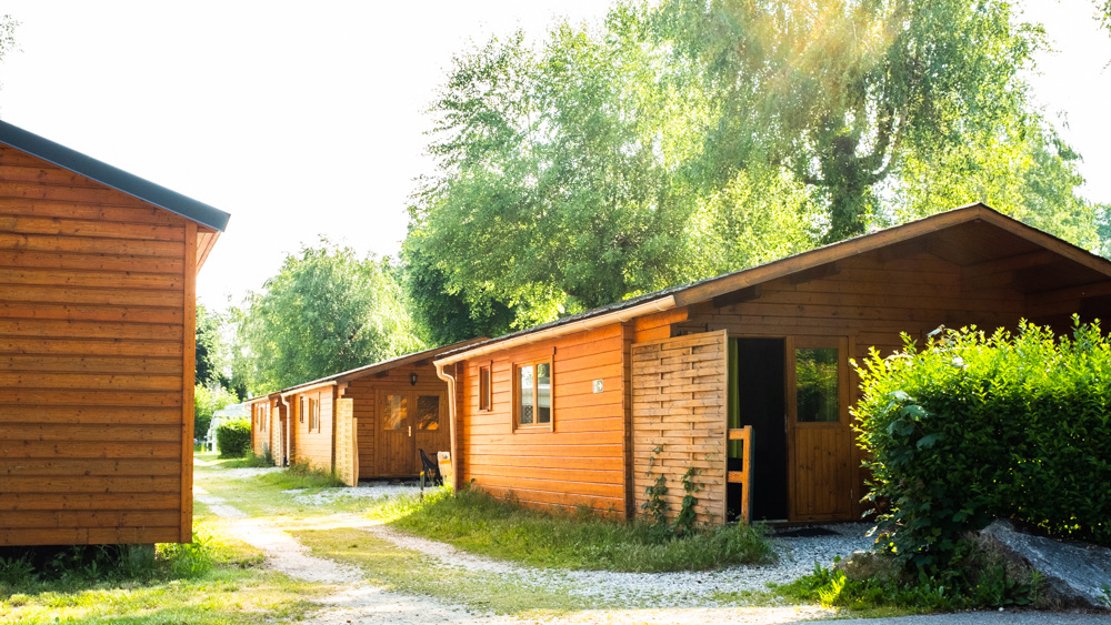 Quatre chalets en bois en location au camping. Dont un chalet PMR, accessible pour les personnes à mobilité réduite. Sous l'ombre des arbres.