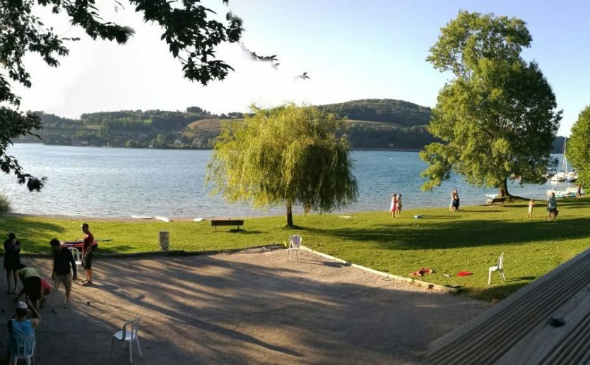 Vue de la plage de Bilieu au bord du lac de Paladru. Terrain de pétanque et baigneurs.